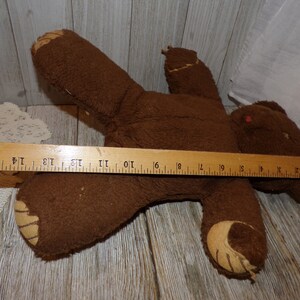 May include: A brown teddy bear with a worn, fuzzy texture. The bear is lying on its back with its arms outstretched. The bear is approximately 46 cm long.