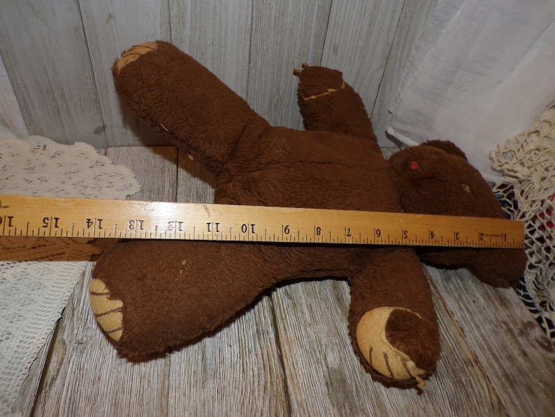 May include: A brown teddy bear with a worn, fuzzy texture. The bear is lying on its back with its arms outstretched. The bear is approximately 46 cm long.