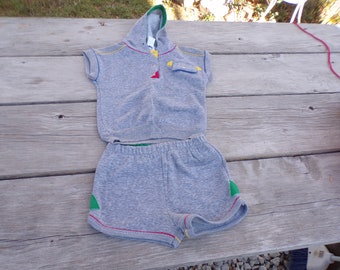 May include: A gray hooded sweatshirt and matching shorts set for a child. The set has colorful trim and a small pocket on the front of the sweatshirt.
