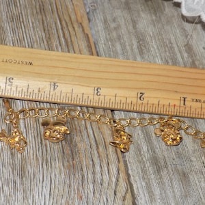May include: Gold charm bracelet with Disney-themed charms, including Mickey Mouse and Donald Duck. The bracelet, displayed on wood, has charms of various characters. The bracelet is approximately 12.7 cm long.