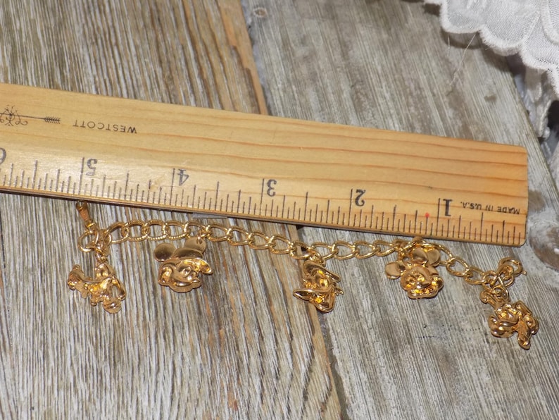 May include: Gold charm bracelet with Disney-themed charms, including Mickey Mouse and Donald Duck. The bracelet, displayed on wood, has charms of various characters. The bracelet is approximately 12.7 cm long.