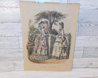 May include: A vintage print titled LA MODE ILLUSTREE featuring two figures in detailed nineteenth-century attire. One figure holds a dark parasol, while the other wears a blue hat. They stand near a stone structure in a garden setting.