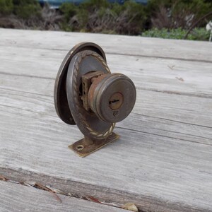 May include: An antique door knob with a keyhole, made of metal with a rusted finish. The knob has an oval backplate and a decorative rope-like design around the edges. The base is a rectangular shape with screw holes.