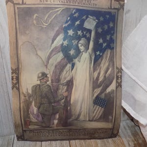 May include: A vintage print with a patriotic theme, showing an American flag and a robed figure holding a document. A soldier kneels in front of the figure. The print has a sepia tone and includes text at the top and bottom.