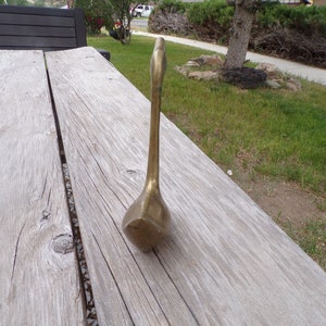 Pu&ograve; includere: Una statuetta di cigno in metallo dorato con un collo lungo e un corpo arrotondato. Il cigno &egrave; in piedi su una superficie di legno.