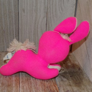 May include: A pink plush bunny rabbit toy with white fur accents. The bunny is lying on its side with its head turned to the side. The bunny has long ears and a fluffy tail.