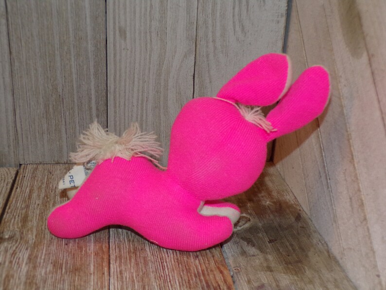 May include: A pink plush bunny rabbit toy with white fur accents. The bunny is lying on its side with its head turned to the side. The bunny has long ears and a fluffy tail.