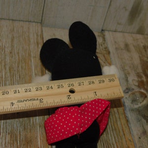 May include: Black and white plush toy mouse wearing a red and white polka dot dress. The toy is approximately 7 inches tall and is measured with a ruler.