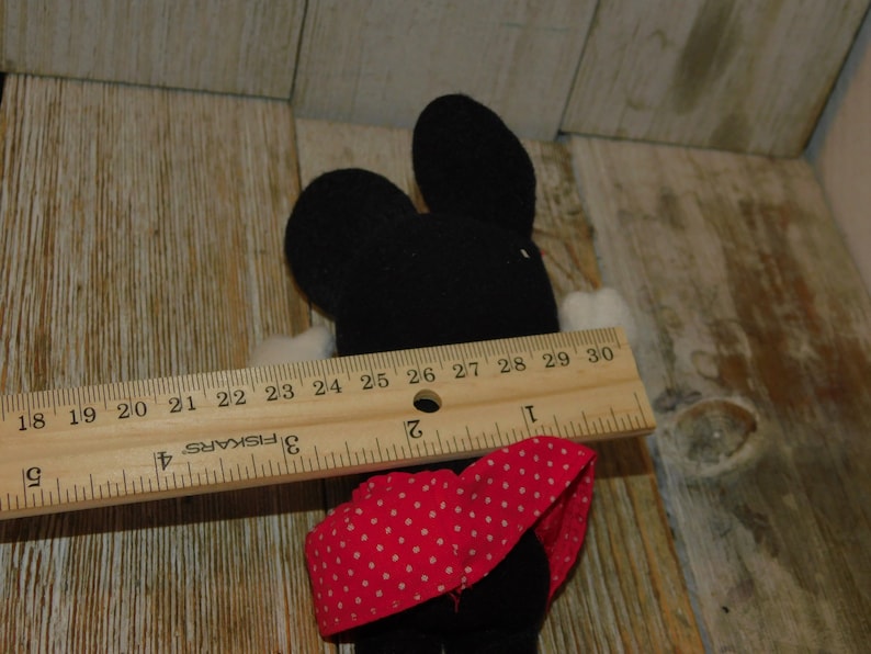 May include: Black and white plush toy mouse wearing a red and white polka dot dress. The toy is approximately 7 inches tall and is measured with a ruler.
