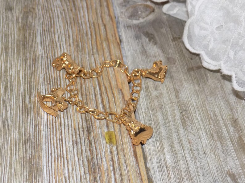 May include: A gold charm bracelet with four charms: a rocking horse, a bell, a carriage, and a shoe. The bracelet is shown on a weathered wooden surface, with white lace in the background.