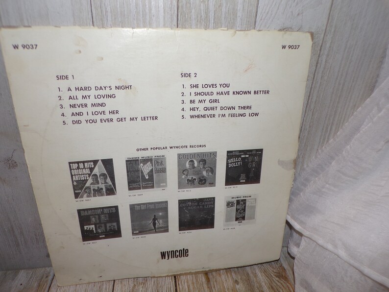 Puede incluir: Una portada de &aacute;lbum de vinilo blanco con texto negro. El &aacute;lbum se titula "The Beatles" y presenta los t&iacute;tulos de las canciones "A Hard Day's Night", "All My Loving", "Never Mind", "And I Love Her", "Did You Ever Get My Letter", "She Loves You", "I Should Have Known Better", "Be My Girl", "Hey, Quiet Down There" y "Whenever I'm Feeling Low".