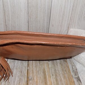May include: A brown leather clutch bag with a zipper closure and a tassel. The bag has a worn look and is made of a soft, supple leather.
