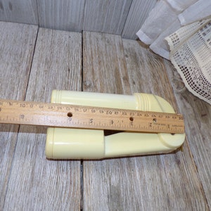 May include: A white plastic garlic press with a handle and a rotating mechanism. The press is about 7 inches long and is sitting on a wooden surface.