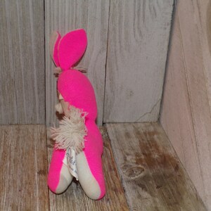 May include: Pink knitted bunny rabbit plush toy with a white fluffy tail. The toy has a white tag with the text "Little Lamb" on it.