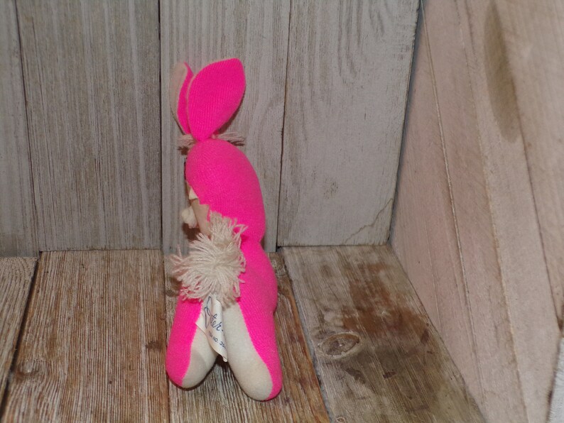 May include: Pink knitted bunny rabbit plush toy with a white fluffy tail. The toy has a white tag with the text "Little Lamb" on it.