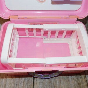 Puede incluir: Cuna de juguete de pl&aacute;stico rosa con barrotes blancos y un colch&oacute;n rosa. La cuna est&aacute; dentro de una maleta de transporte de pl&aacute;stico rosa con un dise&ntilde;o floral.