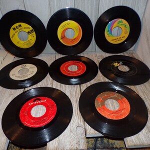 May include: Eight vintage 45 rpm vinyl records with different labels and artists. The records are black with colorful labels. The labels feature the names of the artists and songs.