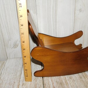 Puede incluir: Una silla mecedora de madera para una mu&ntilde;eca o un ni&ntilde;o peque&ntilde;o. La silla est&aacute; hecha de madera marr&oacute;n claro y tiene un dise&ntilde;o simple. Tiene aproximadamente 38 cm de altura.