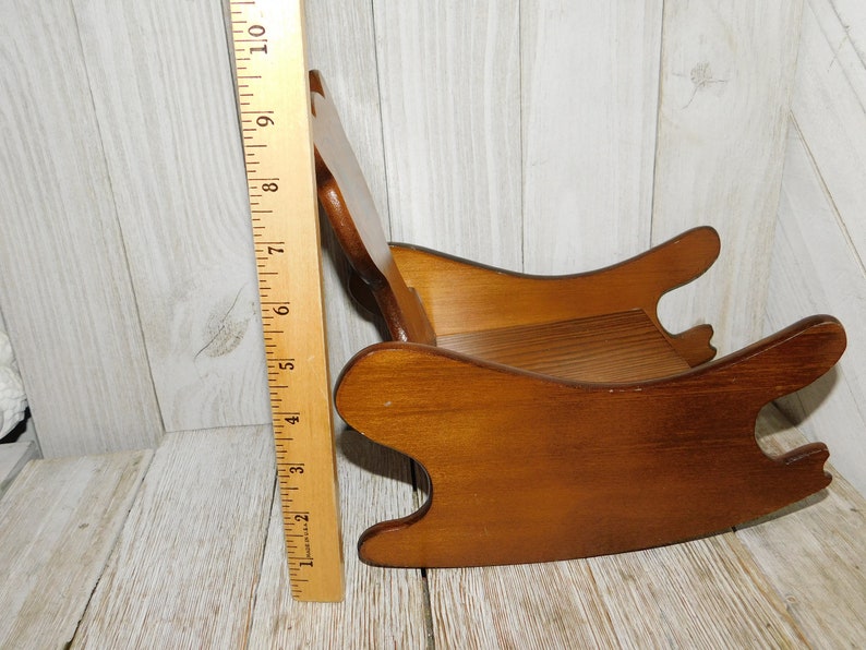 Puede incluir: Una silla mecedora de madera para una mu&ntilde;eca o un ni&ntilde;o peque&ntilde;o. La silla est&aacute; hecha de madera marr&oacute;n claro y tiene un dise&ntilde;o simple. Tiene aproximadamente 38 cm de altura.