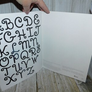 May include: A white page with a black alphabet printed in a cursive font with swirls. The letters are arranged in alphabetical order.