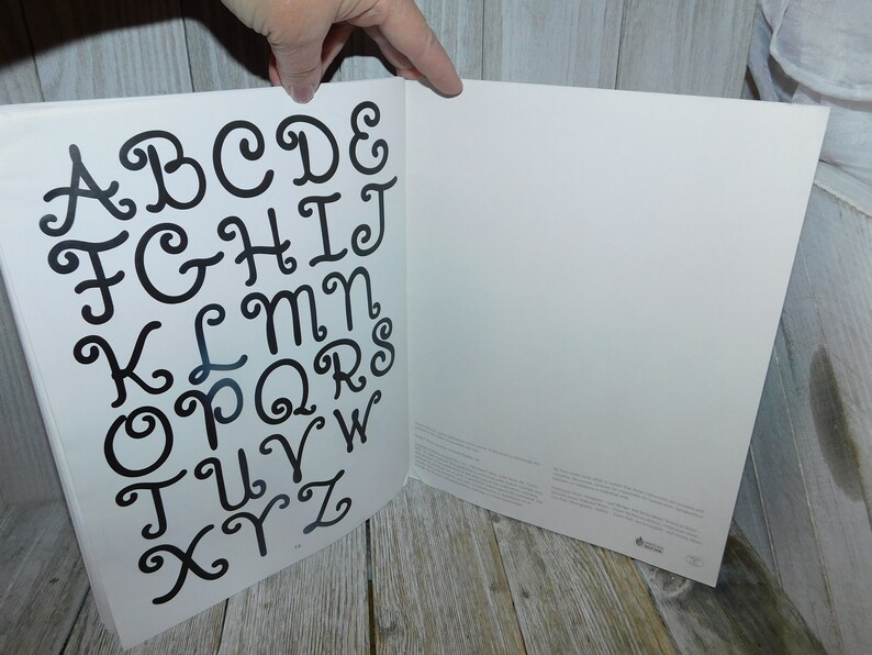 May include: A white page with a black alphabet printed in a cursive font with swirls. The letters are arranged in alphabetical order.