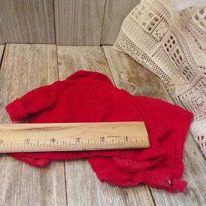 K&ouml;nnte beinhalten: Rote Cord-Samt-Puppenkleidung, ein Pullover und eine Hose, auf einer Holzoberfl&auml;che mit einem Lineal zum Ma&szlig;stab ausgelegt. Der Pullover hat einen Rei&szlig;verschluss.