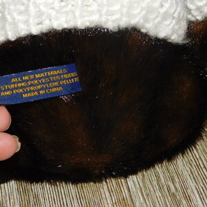 May include: Close-up of a blue label with gold text that reads "All New Materials Stuffing: Polyester Fibres and Polypropylene Pellets Made in China".