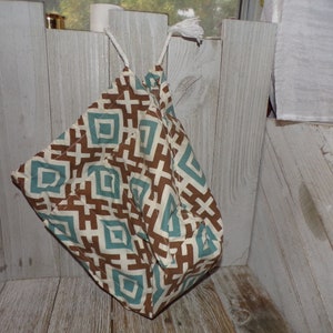 May include: A quilted fabric bag with a geometric pattern in brown, teal, and cream. The bag is suspended by a white cord with a tassel. The pattern features diamond and cross shapes.