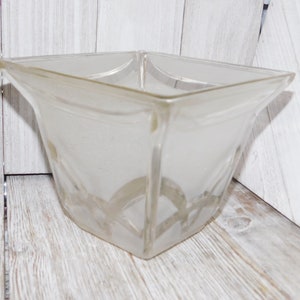 May include: A clear, square glass lampshade with a frosted finish. The lampshade has a flared shape and a decorative, repeating arched pattern near the bottom. The lampshade is designed to diffuse light and add a touch of elegance to any room.