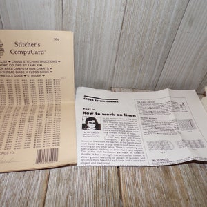 May include: A close-up of a cross stitch instruction booklet with a chart of DMC colors and a section on how to work on linen. The booklet is folded and has a white background with black text.