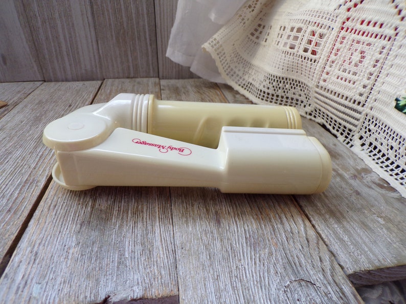 May include: A pair of off-white plastic body massagers with the words "Body Massager" printed in pink on one of the massagers.
