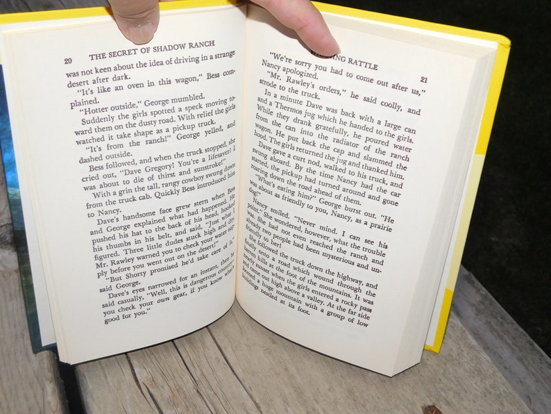May include: Open book with yellow pages showing a scene from a novel about a ranch. The text on the page reads "The Secret of Shadow Ranch" and "We're sorry you had to come out after us."