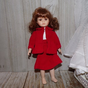 K&ouml;nnte beinhalten: Eine Porzellanpuppe mit braunen Haaren, die eine rote Cordjacke und einen Rock tr&auml;gt.