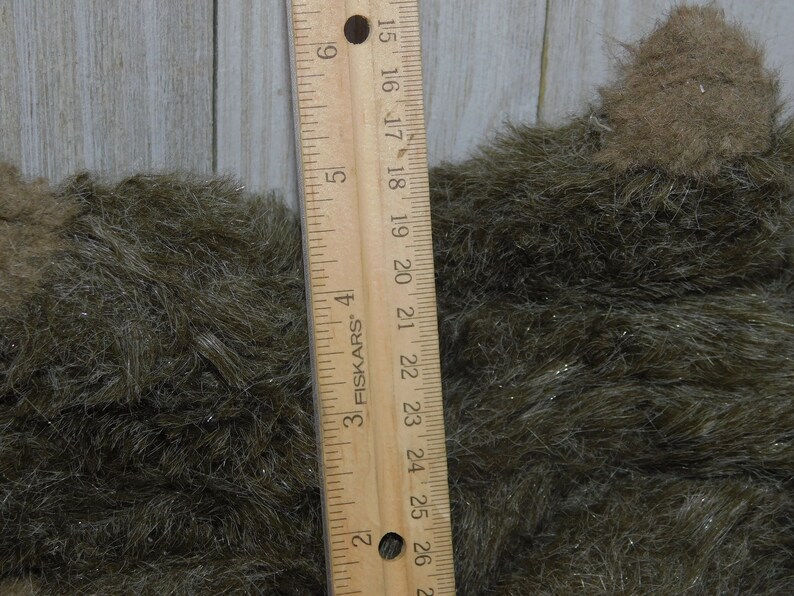 Puede incluir: Primer plano de una tela peluda marr&oacute;n y verde con una regla que mide 66 cm. La tela tiene un brillo sutil.