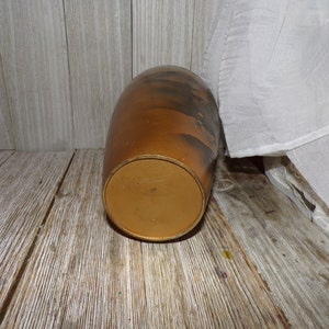 May include: A brown ceramic vase with a gold rim and a black and white design. The vase is sitting on a wooden surface.