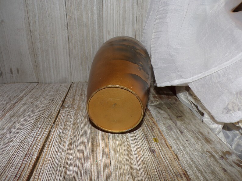 May include: A brown ceramic vase with a gold rim and a black and white design. The vase is sitting on a wooden surface.