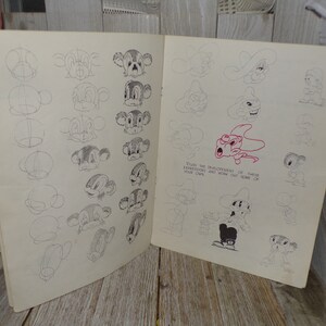 May include: Open book with pencil sketches of cartoon character faces. The sketches show the development of the faces, with step-by-step instructions. The text on the page reads, "Study the development of these expressions and work out some of your own."