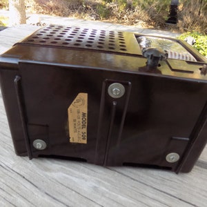 Puede incluir: Una radio vintage marr&oacute;n oscuro con una parte superior perforada y un bot&oacute;n de sintonizaci&oacute;n. La radio tiene una etiqueta que dice "MODEL 509" y "105-125 Volts A.C.-D.C. 30 Watts". Un cl&aacute;sico de la electr&oacute;nica retro.