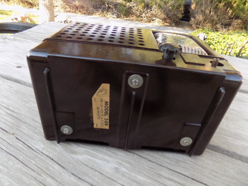 Puede incluir: Una radio vintage marr&oacute;n oscuro con una parte superior perforada y un bot&oacute;n de sintonizaci&oacute;n. La radio tiene una etiqueta que dice "MODEL 509" y "105-125 Volts A.C.-D.C. 30 Watts". Un cl&aacute;sico de la electr&oacute;nica retro.