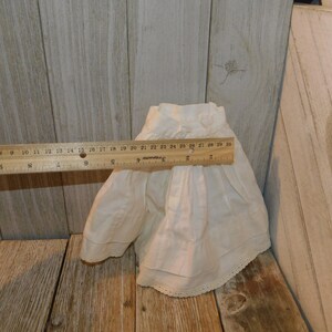 May include: A white cotton doll skirt with a lace trim. The skirt is approximately 76 cm in circumference.