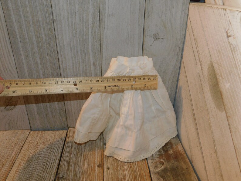 May include: A white cotton doll skirt with a lace trim. The skirt is approximately 76 cm in circumference.