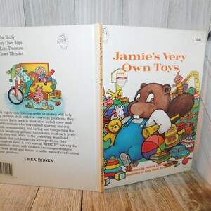 May include: A vintage children's book titled "Jamie's Very Own Toys" features a cartoon illustration of a beaver with a toothy grin, wearing overalls and surrounded by toys. The book cover is yellow and orange with a price tag of $2.95.