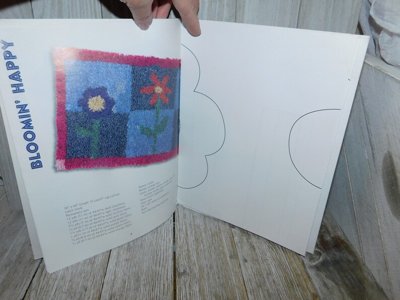 May include: A book titled "Bloom'n Happy" with a colorful rug design on the cover. The rug is made of squares with a red flower, a blue flower, and green leaves. The book is open to a page with a blank template for creating a rug.