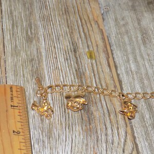 May include: Gold-coloured charm bracelet featuring cartoon character charms. The bracelet includes charms of a rooster, a mouse, and a duck. The bracelet is approximately 18 cm long.