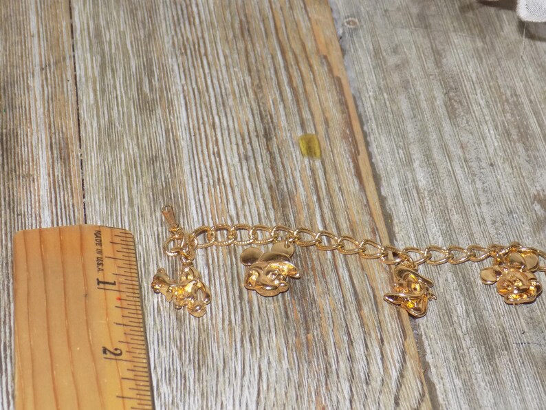 May include: Gold-coloured charm bracelet featuring cartoon character charms. The bracelet includes charms of a rooster, a mouse, and a duck. The bracelet is approximately 18 cm long.