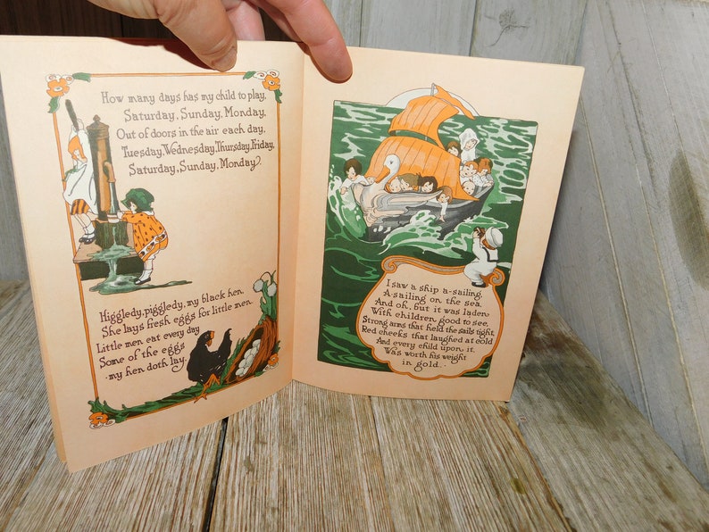 Op de afbeelding: Een open boek met kleurrijke illustraties en tekst. De linkerpagina toont een zwarte hen met eieren en een meisje dat water uit een put pompt. De rechterpagina toont een schip dat op zee vaart met kinderen aan boord. De tekst op de linkerpagina luidt: "Hoeveel dagen heeft mijn kind om te spelen. Zaterdag, zondag, maandag. Elke dag in de frisse lucht. Dinsdag, woensdag, donderdag, vrijdag, zaterdag, zondag, maandag? Higgledy.piggledy, my black hen She lays fresh eggs for little men. Little men ont every day Some of the eggs my hen doth lay." De tekst op de rechterpagina luidt: "Ik zag een schip varen  Varen op zee. En oh, maar het was beladen  Met kinderen, goed om te zien. Sterke armen die de zeilen strak hielden  Rode wangen die lachten in de kou  En elk kind erop  Was zijn gewicht in goud waard."
