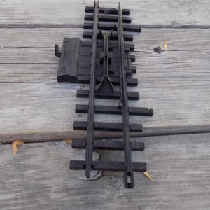 May include: Black plastic model train track switch. The track is set on a wooden surface. The switch allows the train to change direction. The track is made of plastic and has a detailed design.
