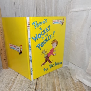 May include: A yellow hardcover book with the title "There's a Wocket in my Pocket!" by Dr. Seuss. The cover features an illustration of a person with a green creature in their pocket.