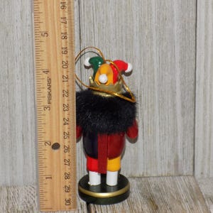 May include: A wooden nutcracker ornament with a red, yellow, and blue jester costume. The nutcracker is wearing a black fur collar and a gold crown. The ornament is approximately 4 inches tall.