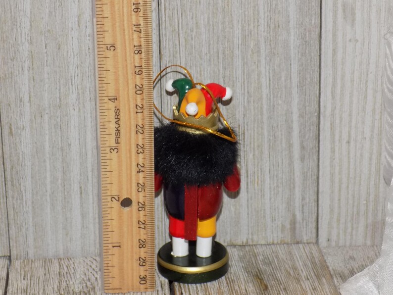 May include: A wooden nutcracker ornament with a red, yellow, and blue jester costume. The nutcracker is wearing a black fur collar and a gold crown. The ornament is approximately 4 inches tall.
